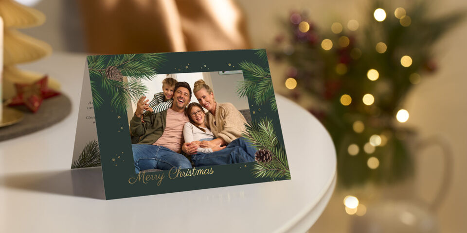 kartka swiateczna CEWE ze zdjeciem rodziny i napisem Merry Christmas postawiona na stole ze swieca w tle rozmyta choinka